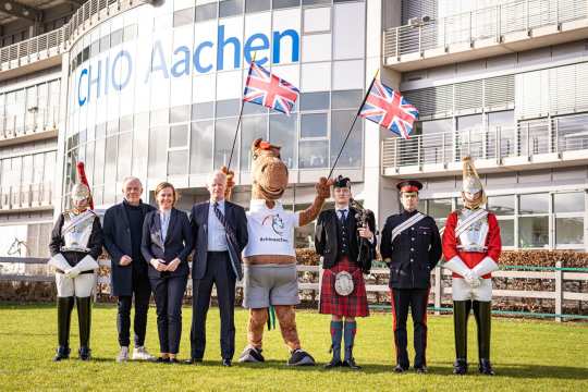 The photo shows representatives of the partner country Great Britain, the CHIO Aachen and mascot Karli. Framed by guards of the Household Cavalry Regiment from left to right: Uwe Brandt, Birgit Rosenberg, Jim Eyre, Karli, bagpiper David Johnston and Daniel Evans. Photo: CHIO Aachen/ Jil Haak