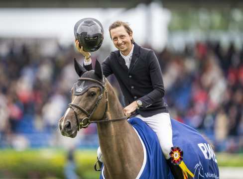 Martin Fuchs mit seinem Helm grüßend und Commissar Pezi mit der blauen Siegerdecke des RWE Preis von Nordrhein-Westfalen bei ihrer Ehrenrunde