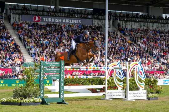 Andre Thieme und seine Fuchsstute Chakaria über einem Oxer mit Rolex Grand Slam Fängen auf der einen Seite und dem CHIO Aachen Logo auf der anderen Seite vor der ausverkauften Tribüne im Hauptstadion