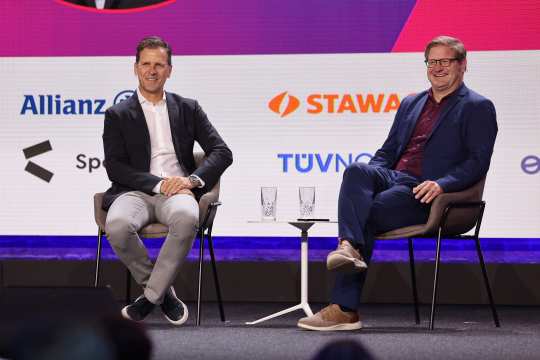 Oliver Bierhoff und Moderator Michael Bröcker sitzen lächelnd auf der Bühne des Kongress #neuland und blicken lächelnd Richtung Publikum.