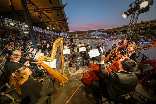 Blick aus der Mitte des Sinfonieorchester Aachen auf die Tänzer in der Mitte des ausverkauften Dressurstadions beim Konzert „Pferd & Sinfonie“