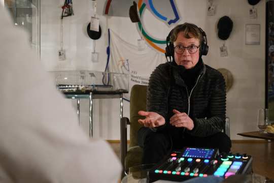 Isabell Werth on an armchair in front of a control desk in the CHIO Aachen Museum gesturing while wearing a headset during the recording of the CHIO Aachen Podcast